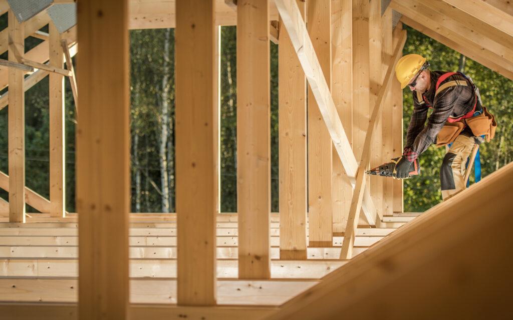 Holzkonstruktion im Rohbau – Bauarbeiter befestigt Teile mit einer Nagelpistole.